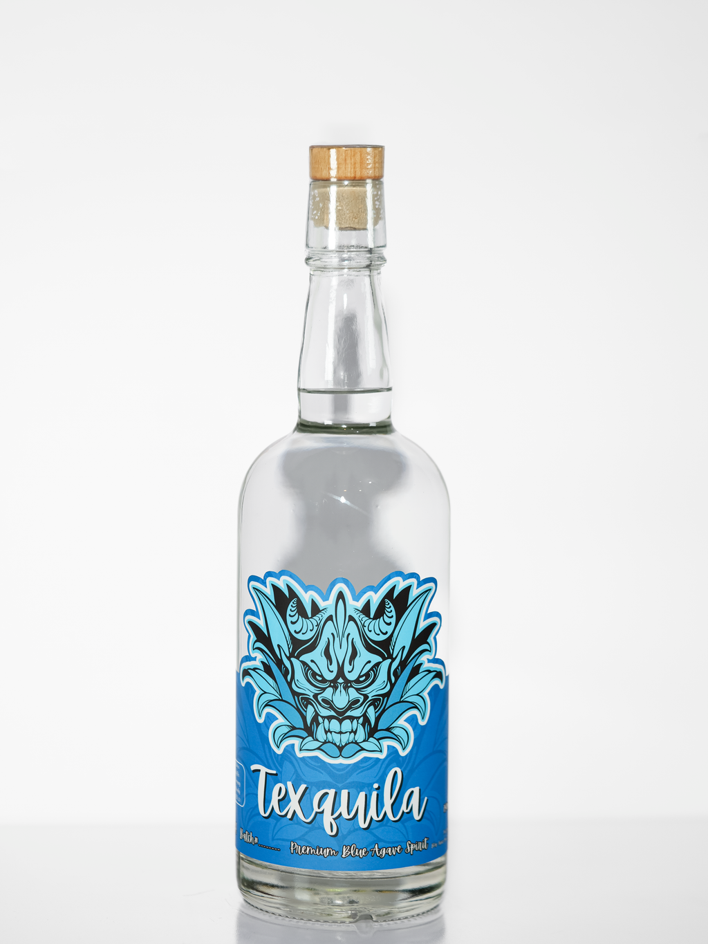 A clear glass bottle of Texquila agave spirit with a cork stopper, featuring a vibrant blue label with a stylized blue and black dragon illustration and white script text.