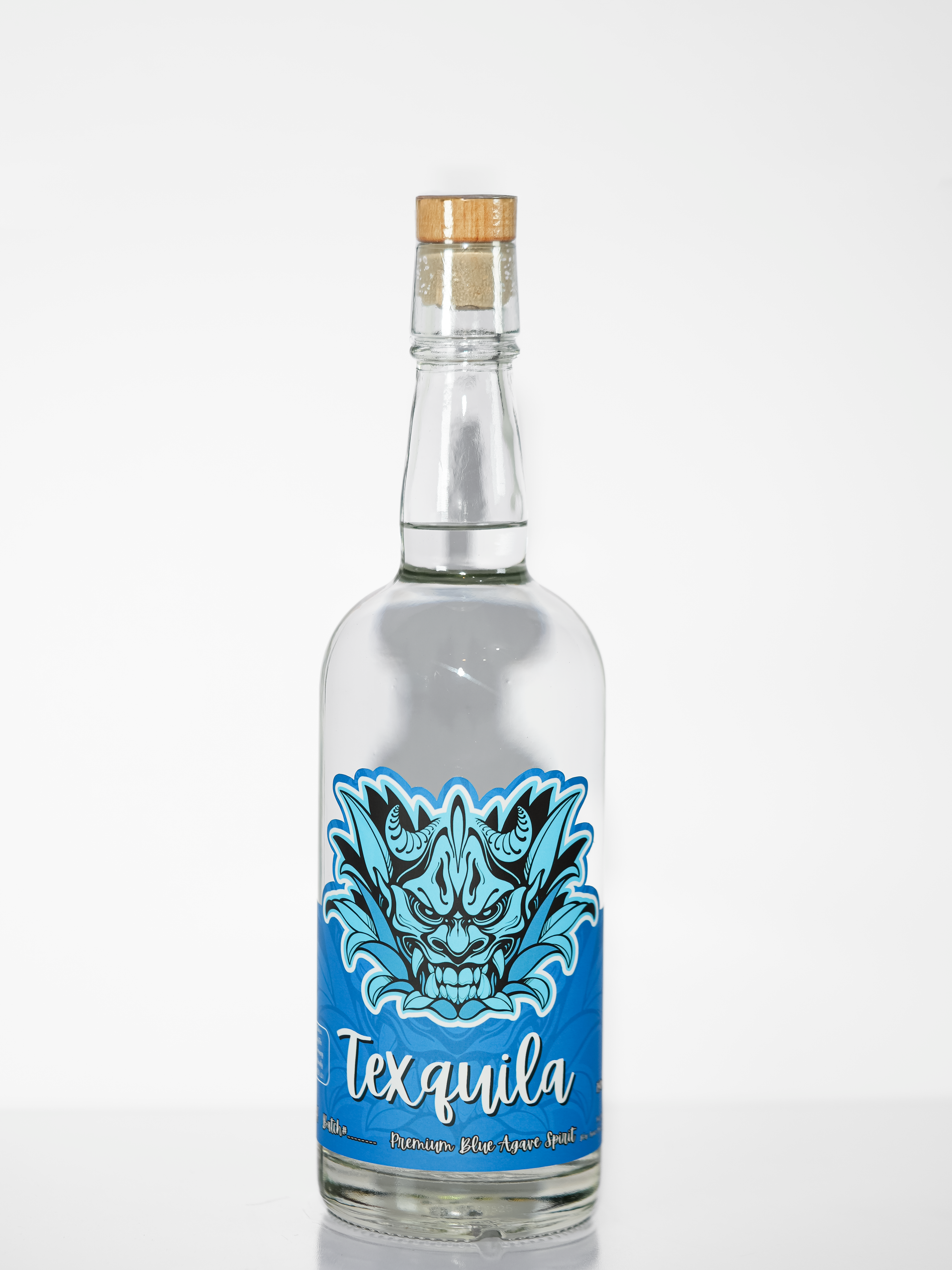 A clear glass bottle of Texquila agave spirit with a cork stopper, featuring a vibrant blue label with a stylized blue and black dragon illustration and white script text.